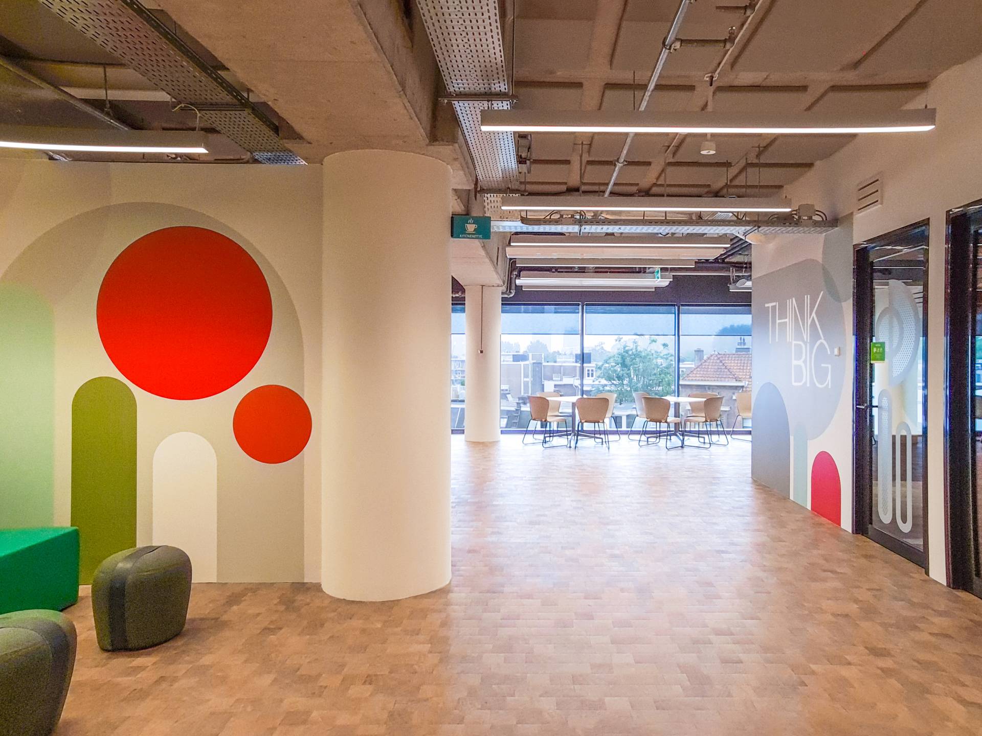 Allée dans les bureaux de chez Instant Group, salle de réunion dans le fond avec de grandes baies vitrées, espace cosy sur la gauche avec des poufs colorées