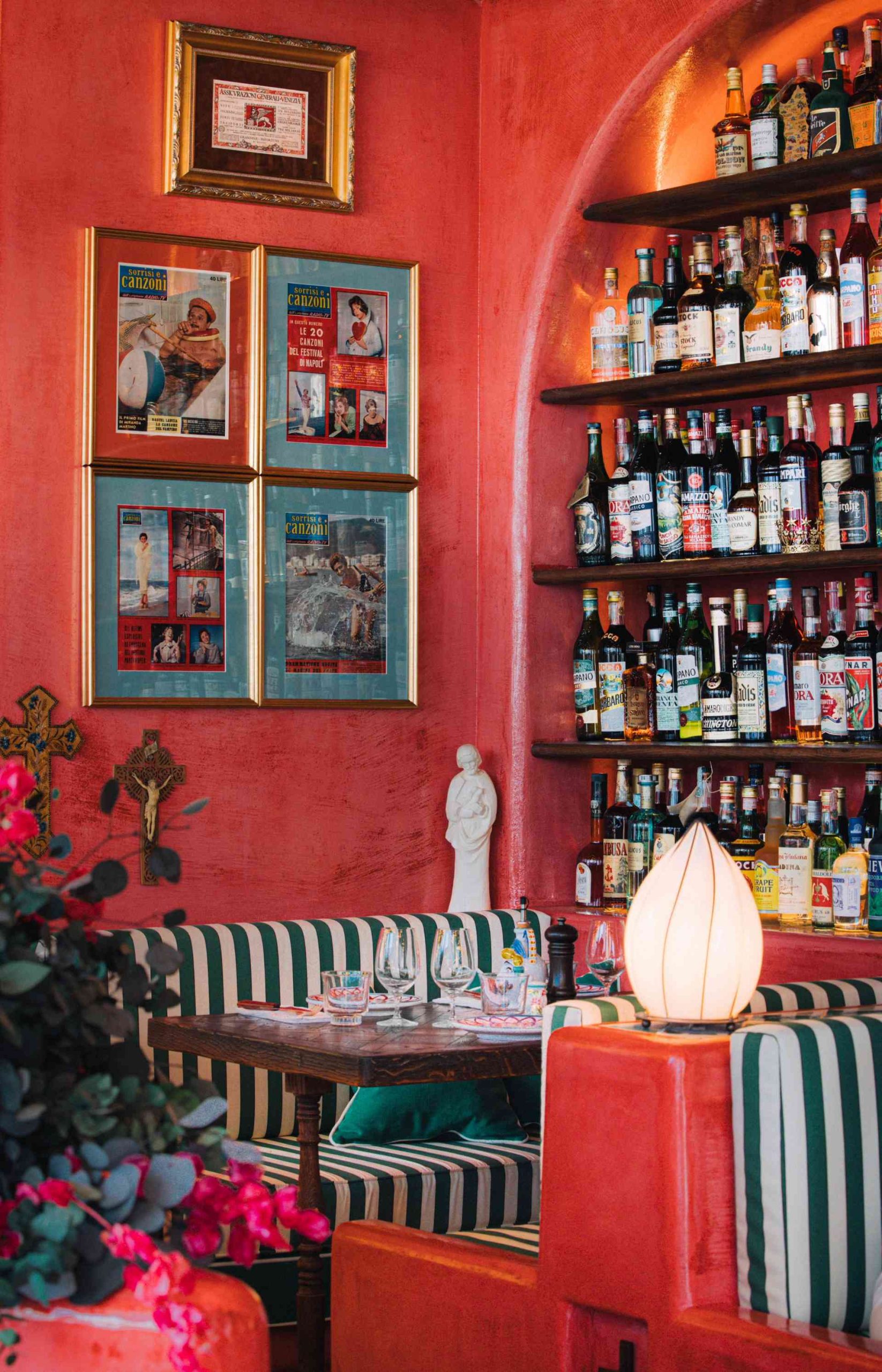 Espace dans le restaurant avec banquette rayée blanche et verte, étagère avec présentation de bouteilles, les murs peint en rouge