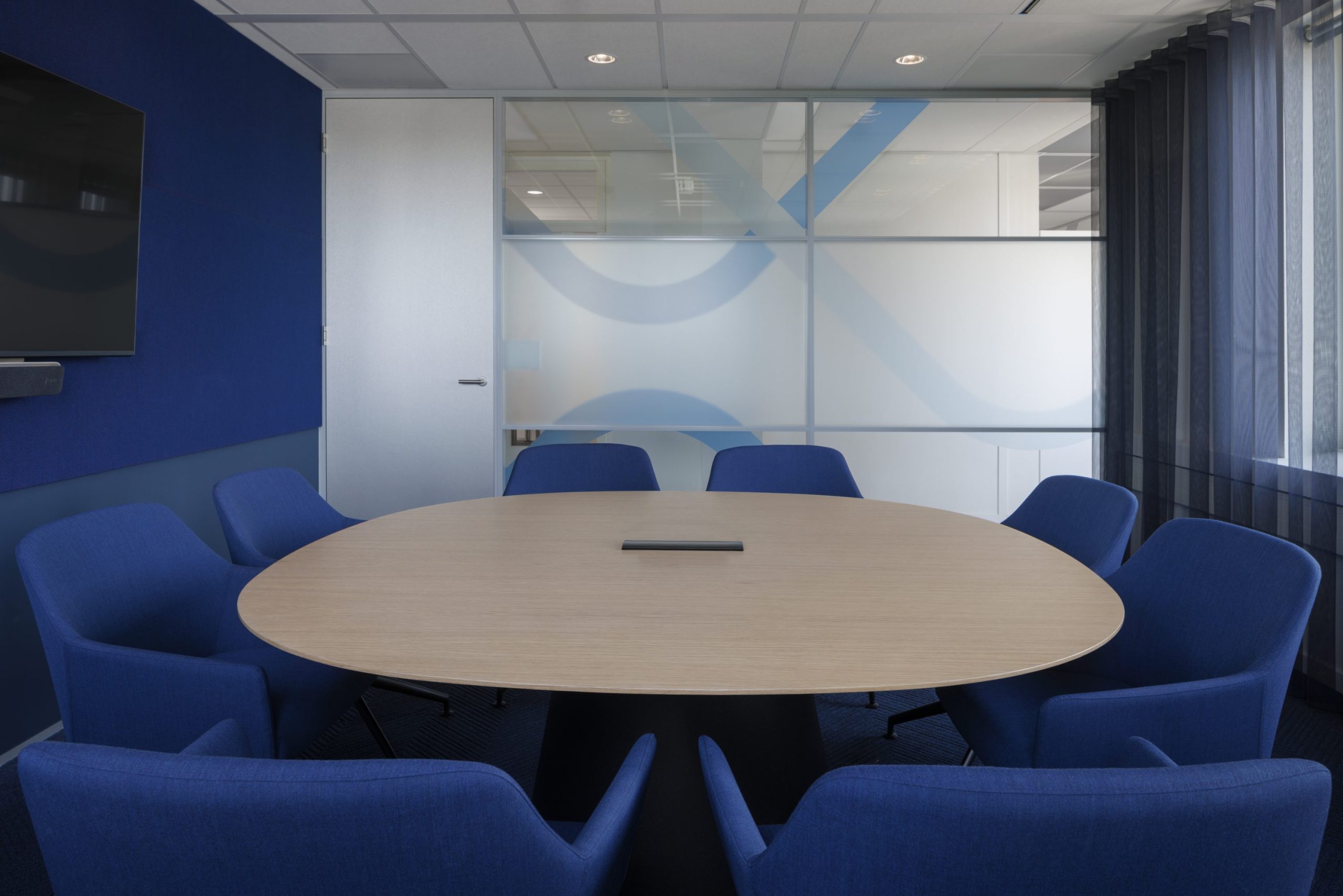 Salle de réunion pour 8 personnes avec table ovale en bois clair et fauteuils bleus foncés