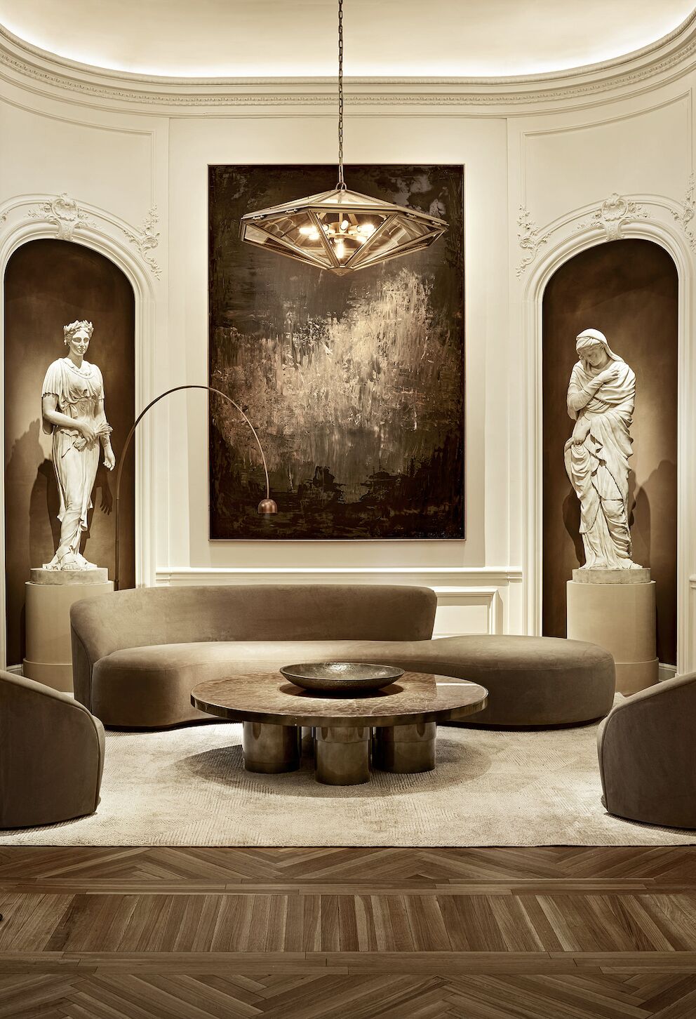 Petit salon arrondi, avec dans canapé, table basse ronde, et 2 grandes alcôves avec statues sur les côtés - RH