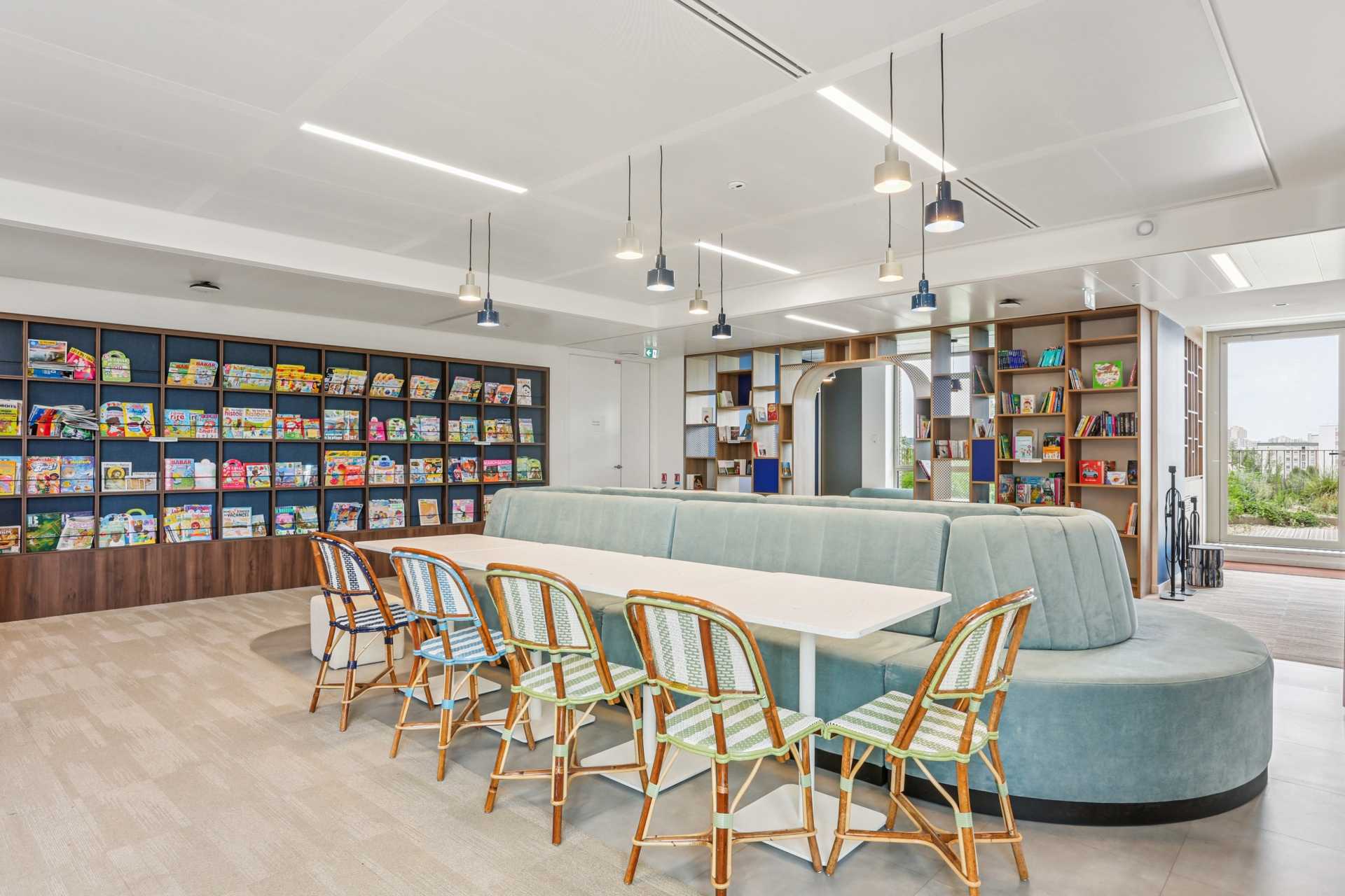 Espace de pause convivial avec une grande banquette bleu gris clair, et une grande bibliothèque sur le mur du fond.
