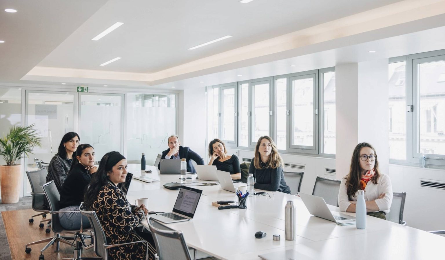 Photo de plusieurs personnes dans une salle de réunion en train de regarder vers un écran ou un orateur principal qui est hors champ.