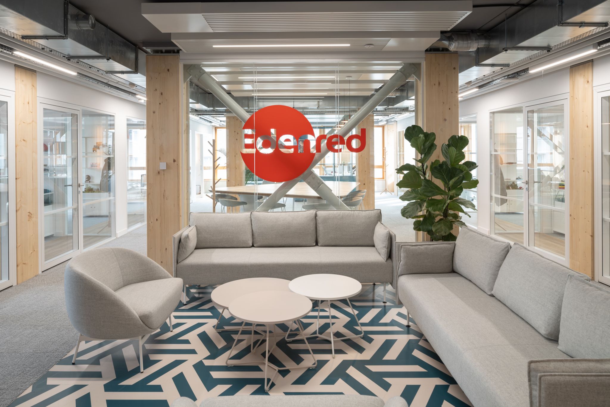 Espace détente cosy avec canapés et fauteuils gris clair. Logo Edenred en vitrophanie derrière