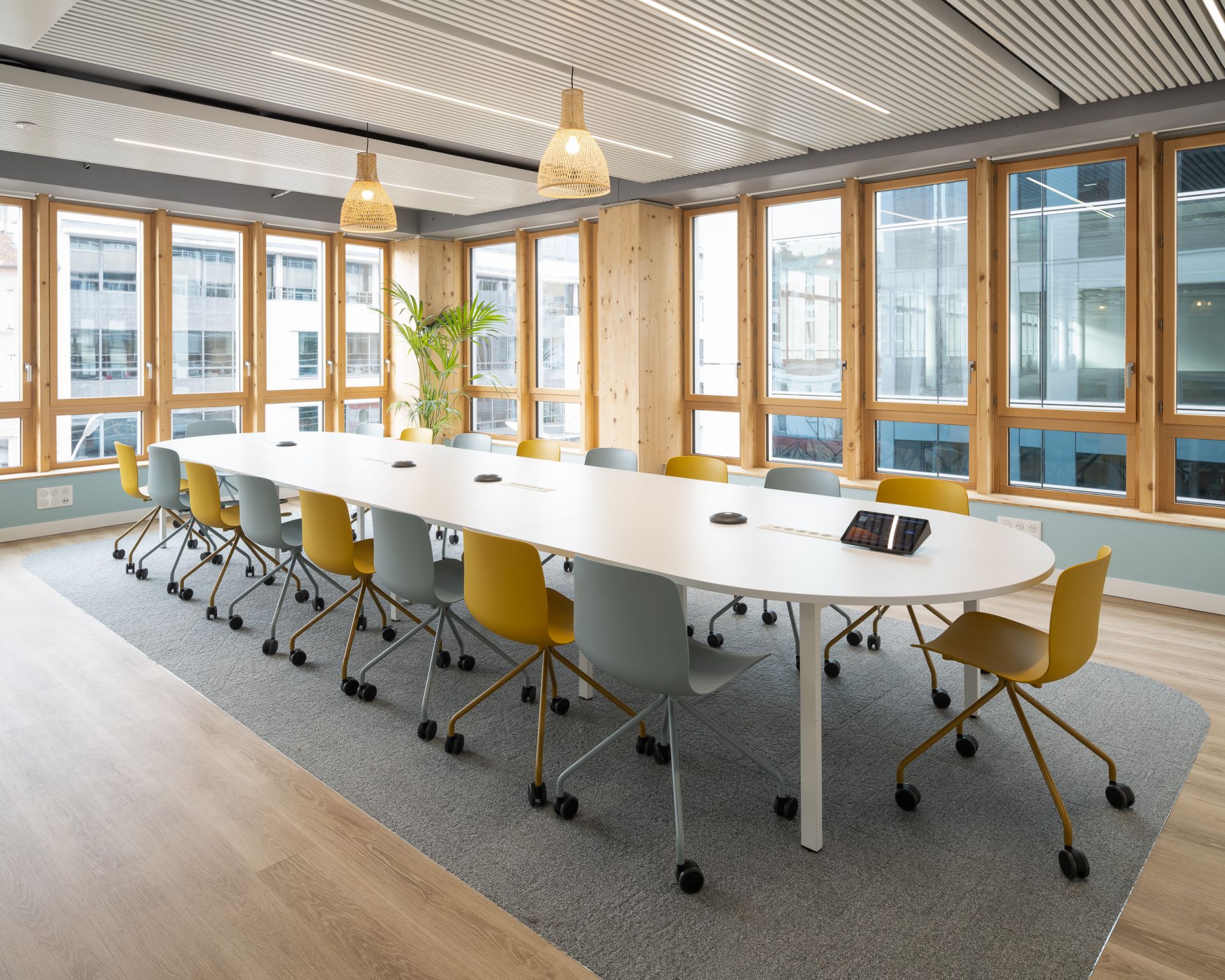 Grande salle de réunion avec des chaises grise et jaune, avec des fenêtres sur 2 murs, apportant un maximum de lumière à la pièce