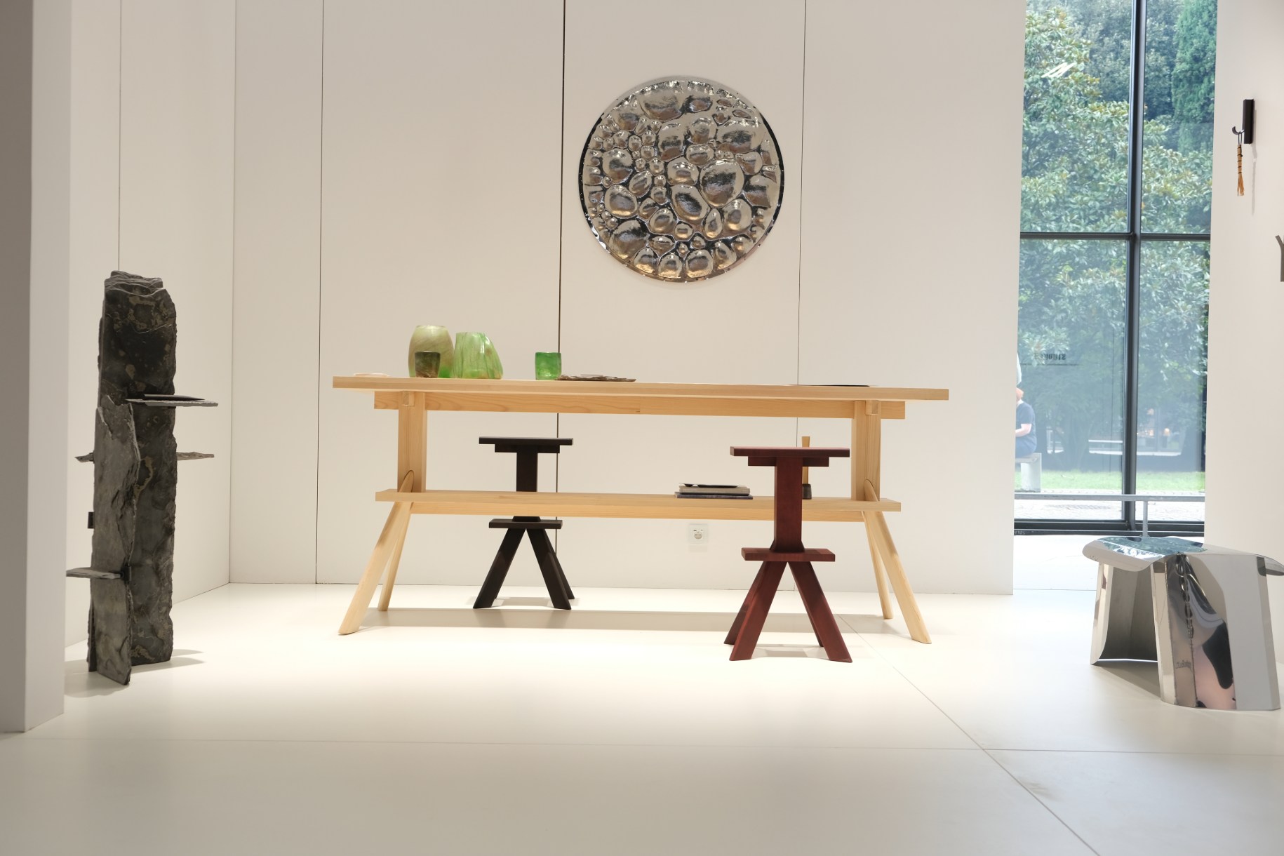 mesa de madera clara, taburete de madera sin tratar, pared blanca y decoración mural de acero