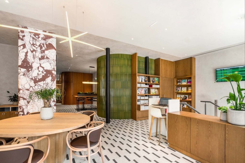 Intérieur du lounge, vu sur une table en bois clair, poutre en marbre, bibliothèque séparative en carrelage vert et aux finitions en bois