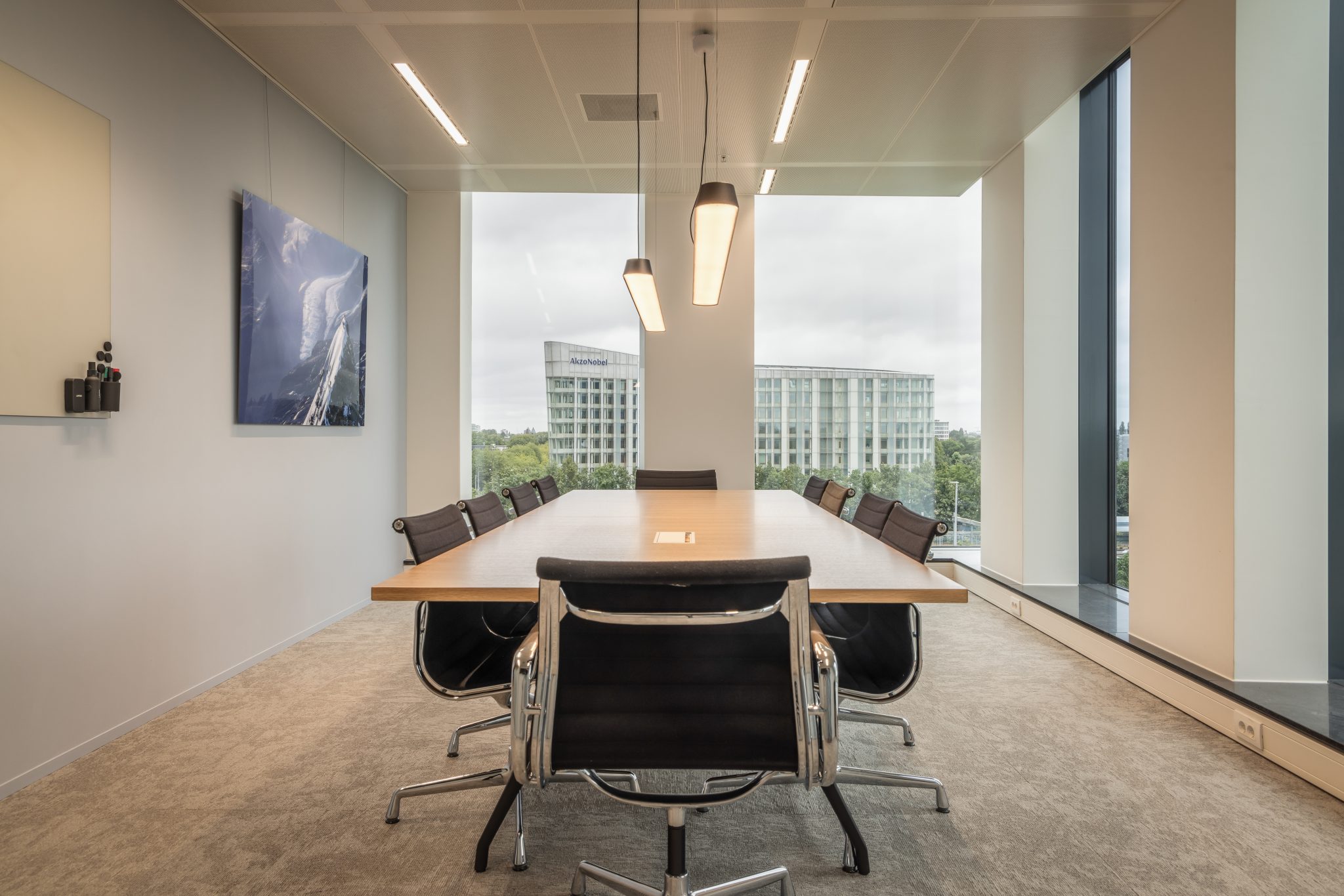 sala de reuniones, mesa de madera clara, silla negra, moqueta gris, ventanal, pared blanca
